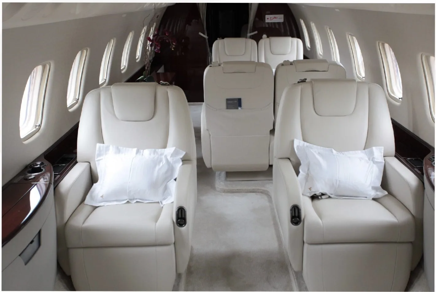 The interior of a private jet cabin with multiple rows of cream-colored leather seats, each with a white pillow.