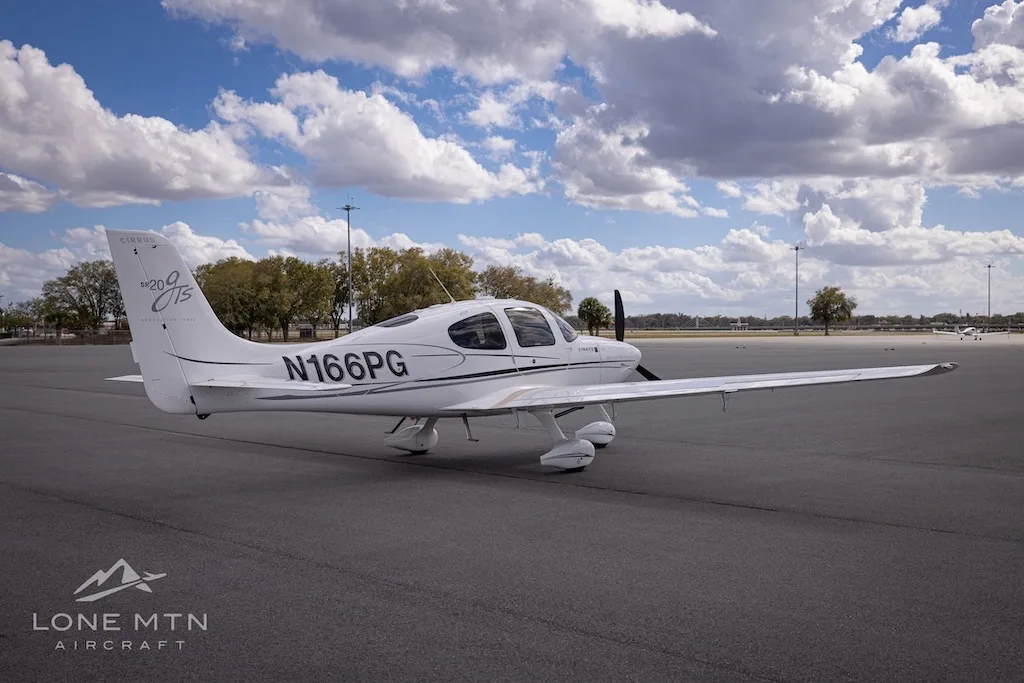 A rear-side view of the white Cirrus SR20 aircraft (N166PG) on an airport tarmac.
