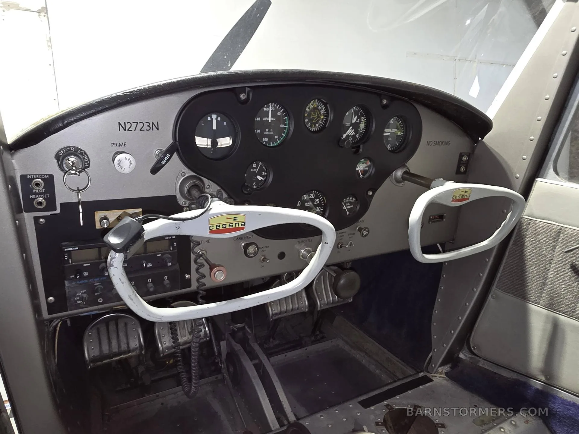 The cockpit of a small aircraft shows the instrument panel with gauges, radio stack, and two control yokes.