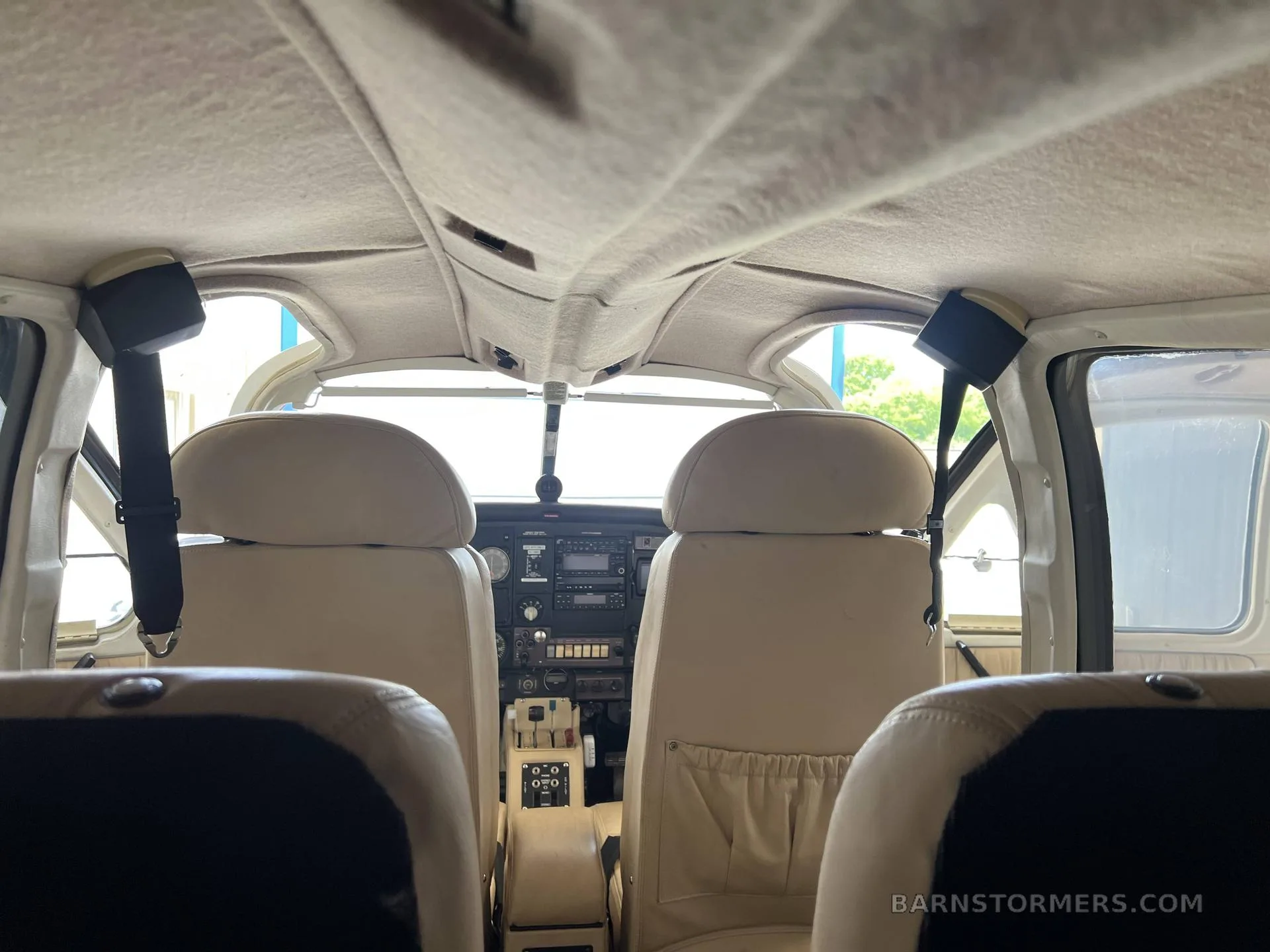 The beige interior cabin of a small aircraft, viewed from the rear seats looking towards the cockpit.