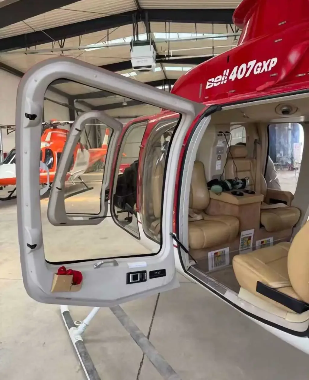 The open door of a red and white Bell 407GXP helicopter reveals its tan leather passenger seats.