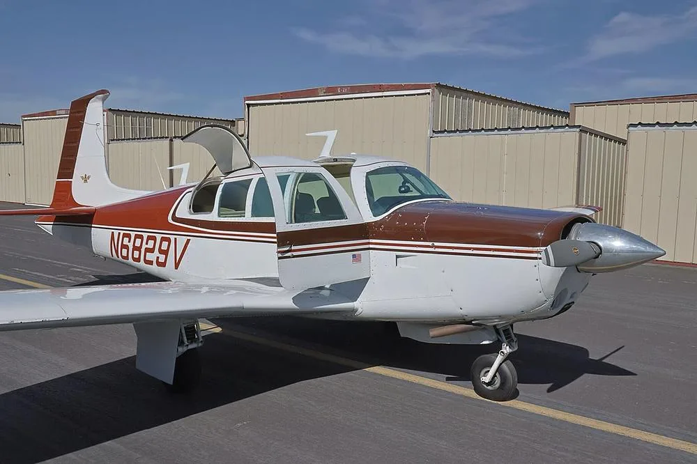 A side view of the brown and white single-engine aircraft, N6829V, with its passenger and baggage doors open on an airfield.