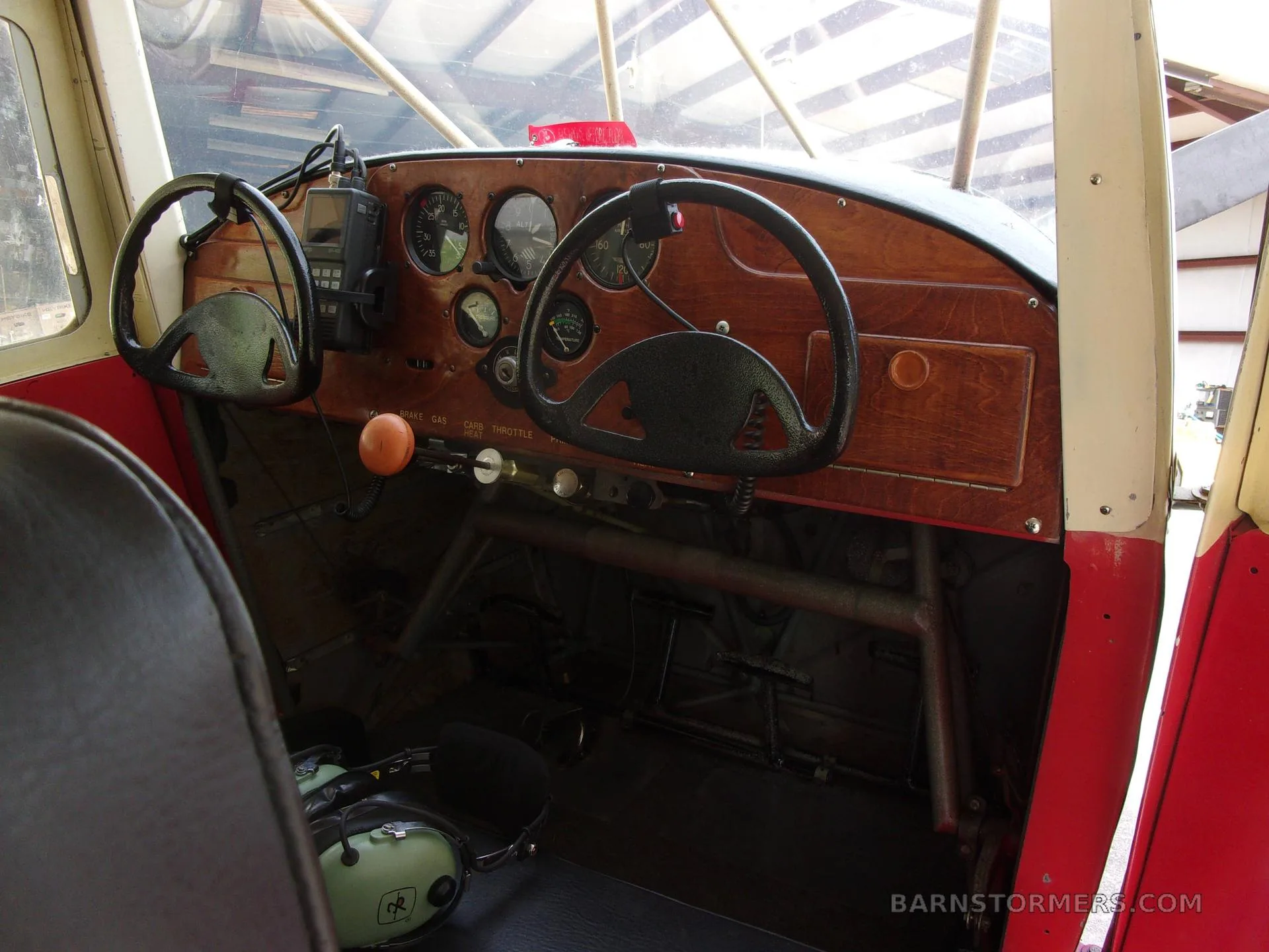 The cockpit of a Taylorcraft BC-12D aircraft, showing a wooden instrument panel with gauges and two control yokes.