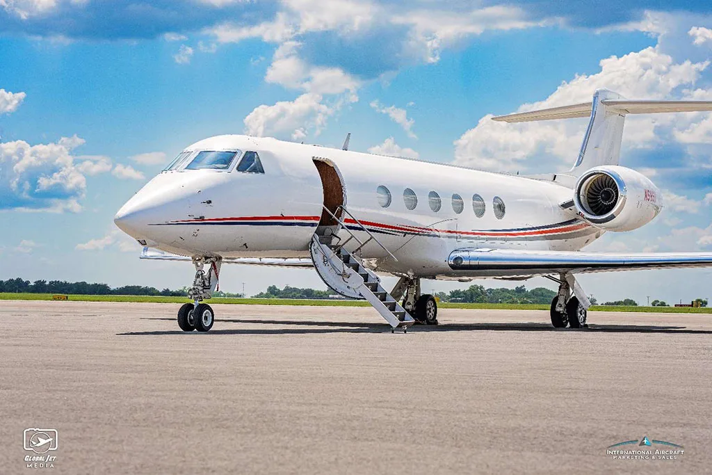 A white Gulfstream G550 aircraft with its main cabin door open and airstairs extended, parked on an airfield.