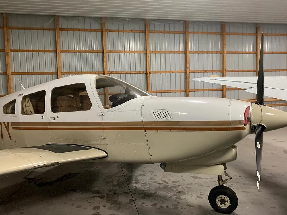 A close-up view of the front fuselage and propeller of the Piper Arrow IV aircraft, N4297Y, in a hangar.