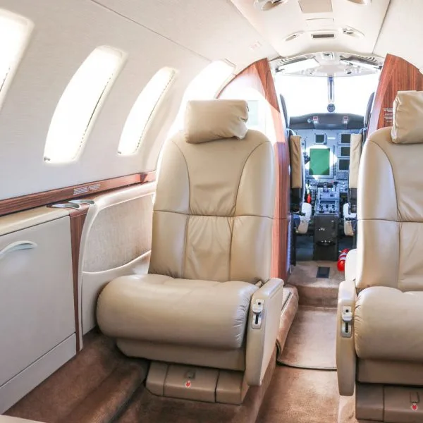 Interior view of an aircraft cabin with beige leather seats, looking towards the cockpit from the side.