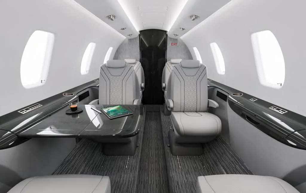 A luxurious aircraft cabin interior with light gray seats, a dark table, and ambient lighting.