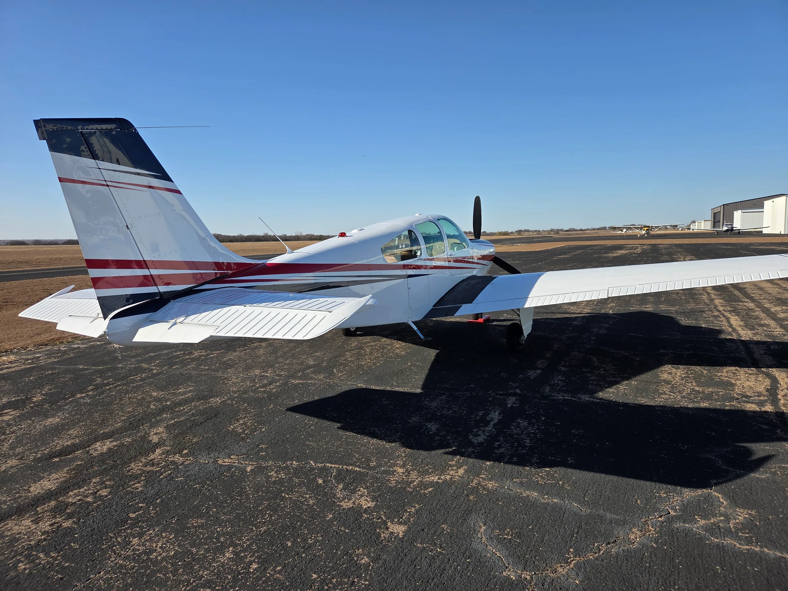 A rear view of a white and red single-engine aircraft with a distinctive tail, parked on an asphalt ramp.