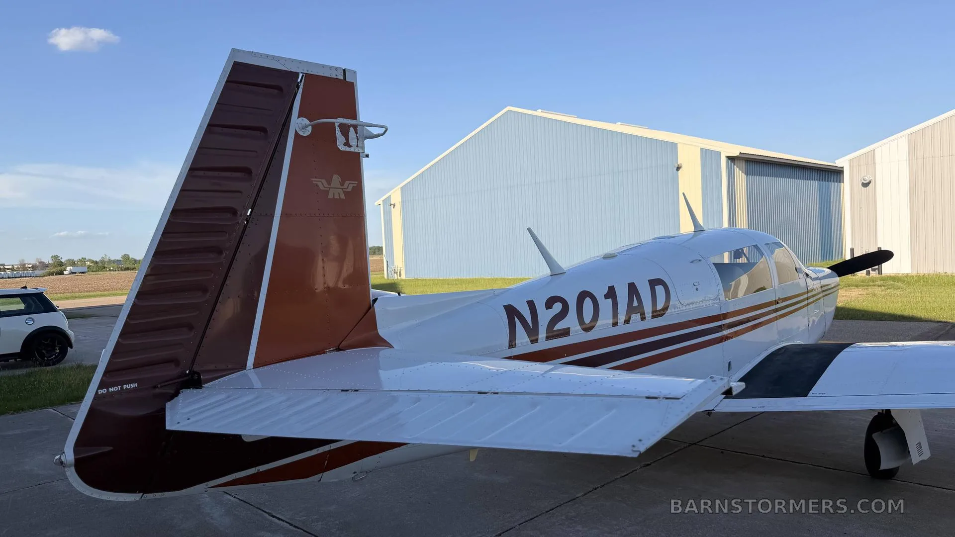 The tail and rear fuselage of a white aircraft with brown stripes, registration N201AD, parked on a tarmac.