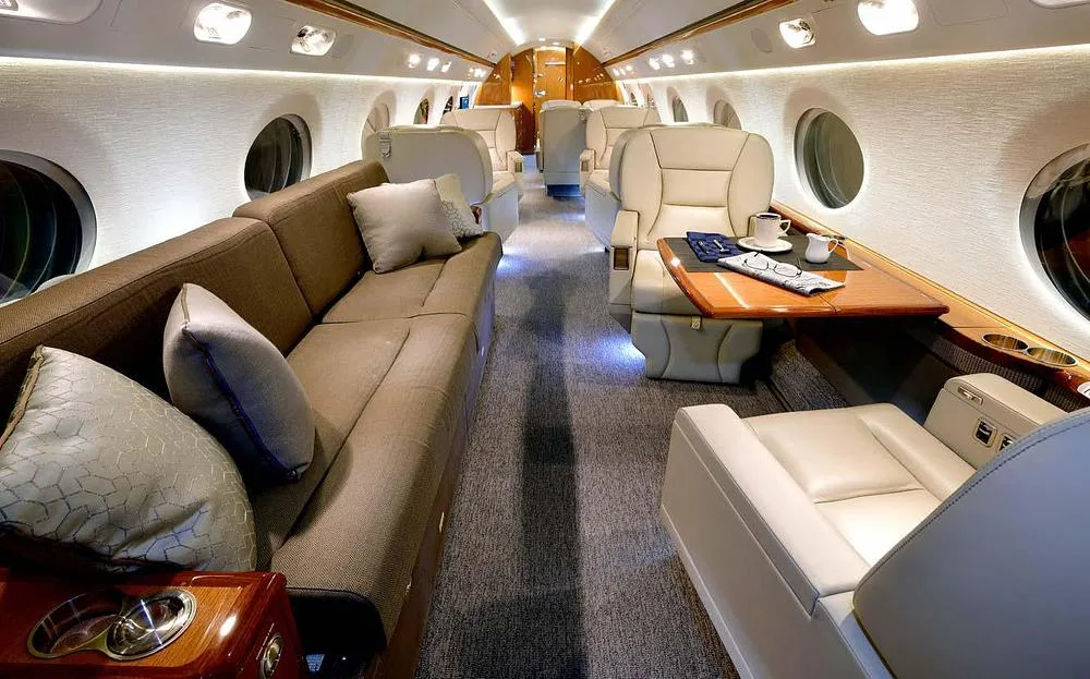 A view inside a private jet cabin featuring a long sofa, individual seats, and a table set with coffee.