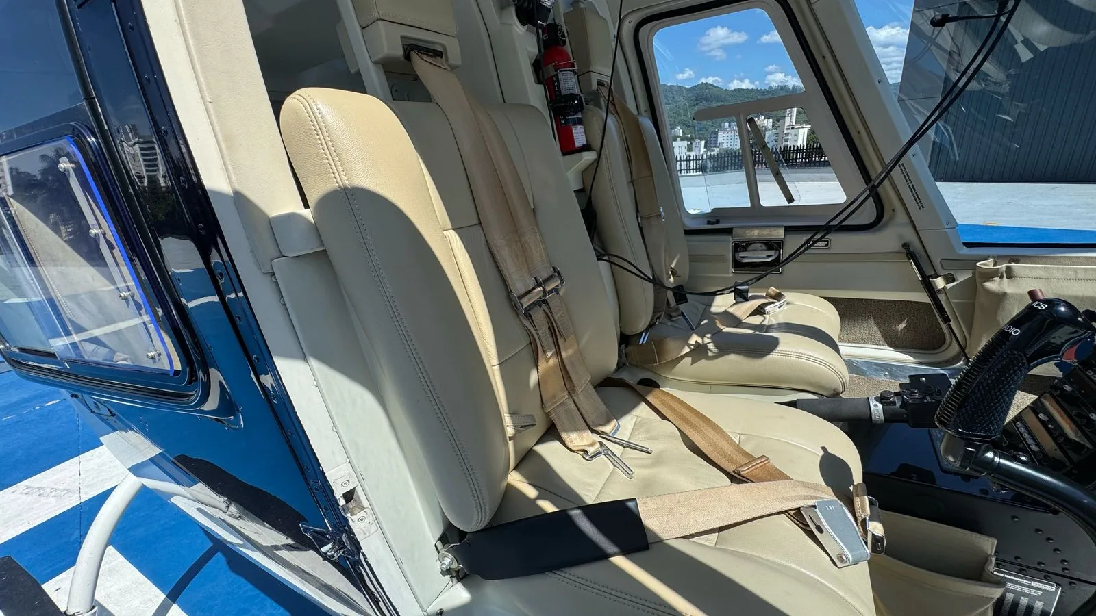 The light tan leather front seats of a helicopter cabin with seatbelts, looking out to a cityscape.