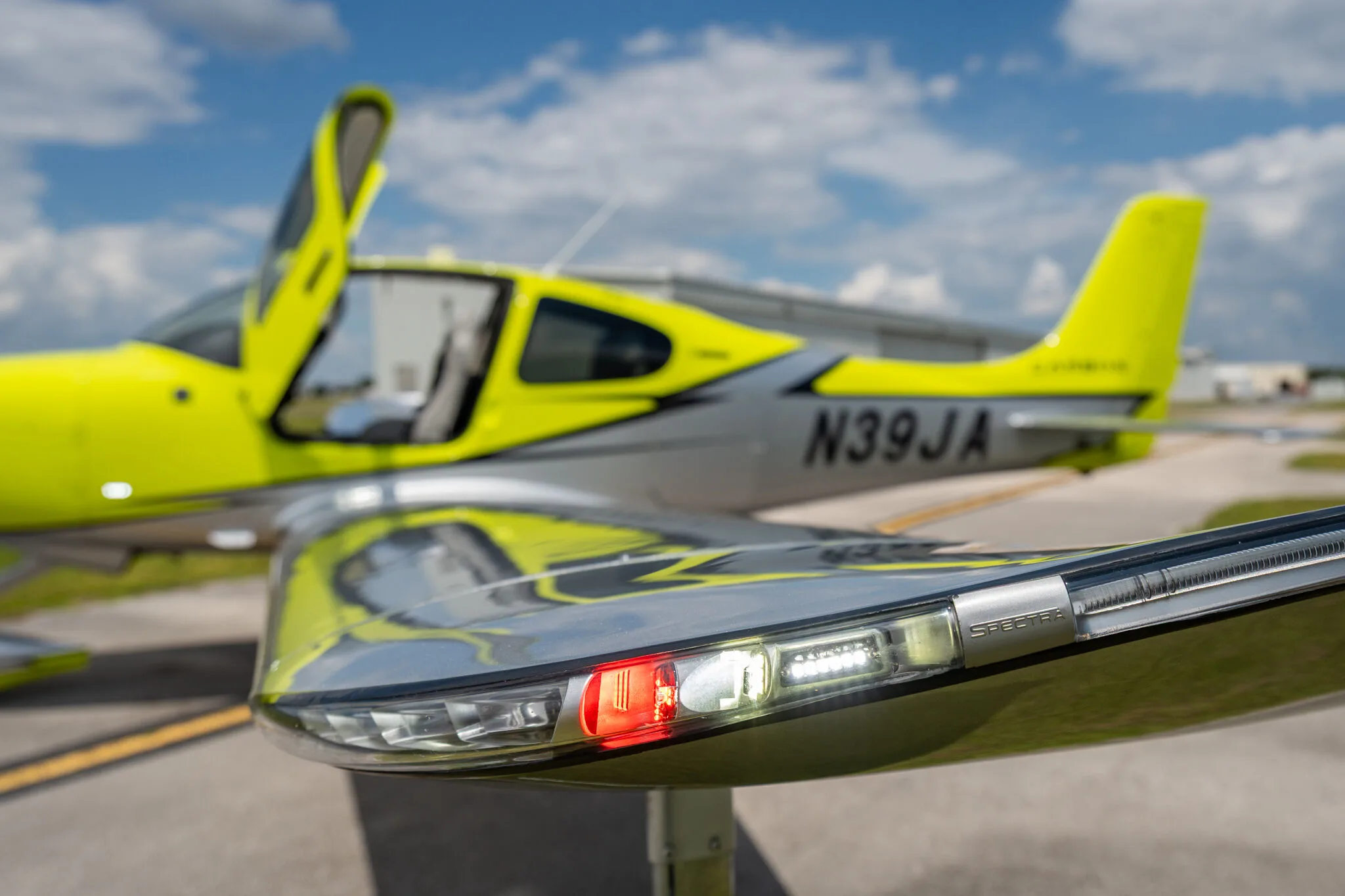Close-up of the right wingtip and fuselage of a lime green and silver Cirrus SR20 aircraft with registration N39JA, showing the navigation lights and open cabin door.
