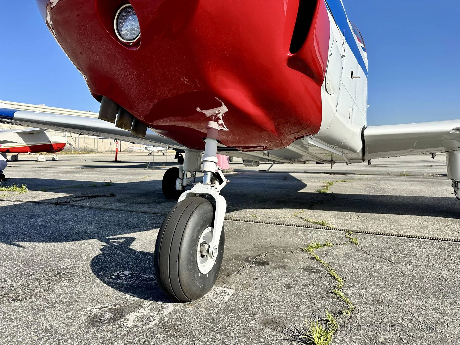A low-angle close-up of the nose landing gear and red underside of a propeller aircraft on a concrete ramp.