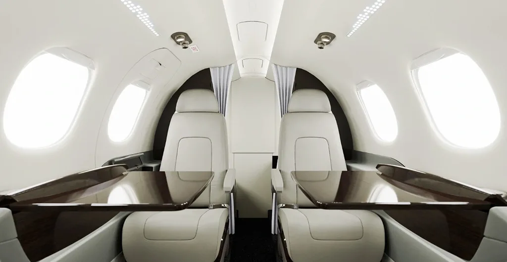 The luxurious interior cabin of a private jet featuring light-colored seats and dark wood tables.