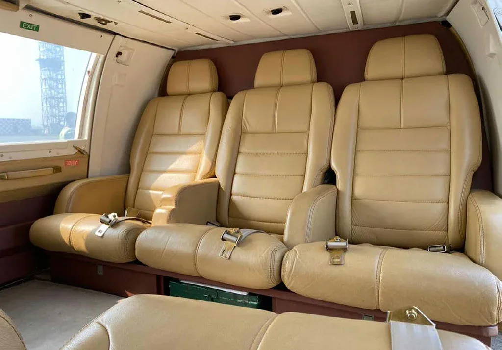 Three tan leather passenger seats in the cabin of a helicopter, with a window showing an exterior structure.