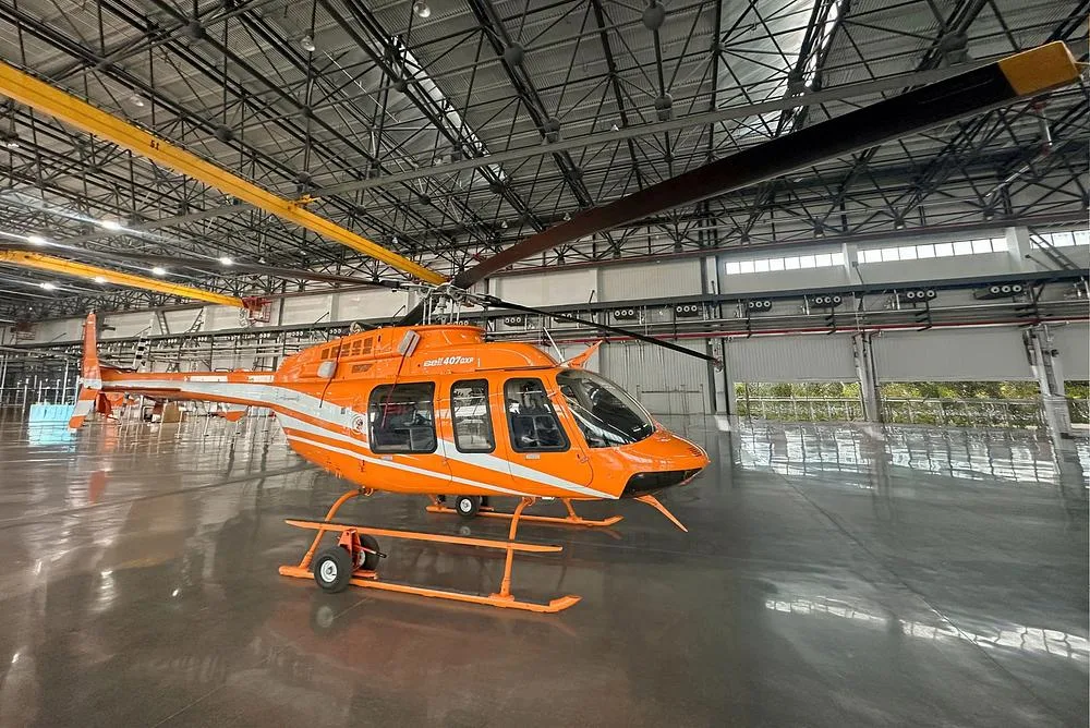 A three-quarter rear view of the orange and white Bell 407GXP helicopter in a spacious hangar.