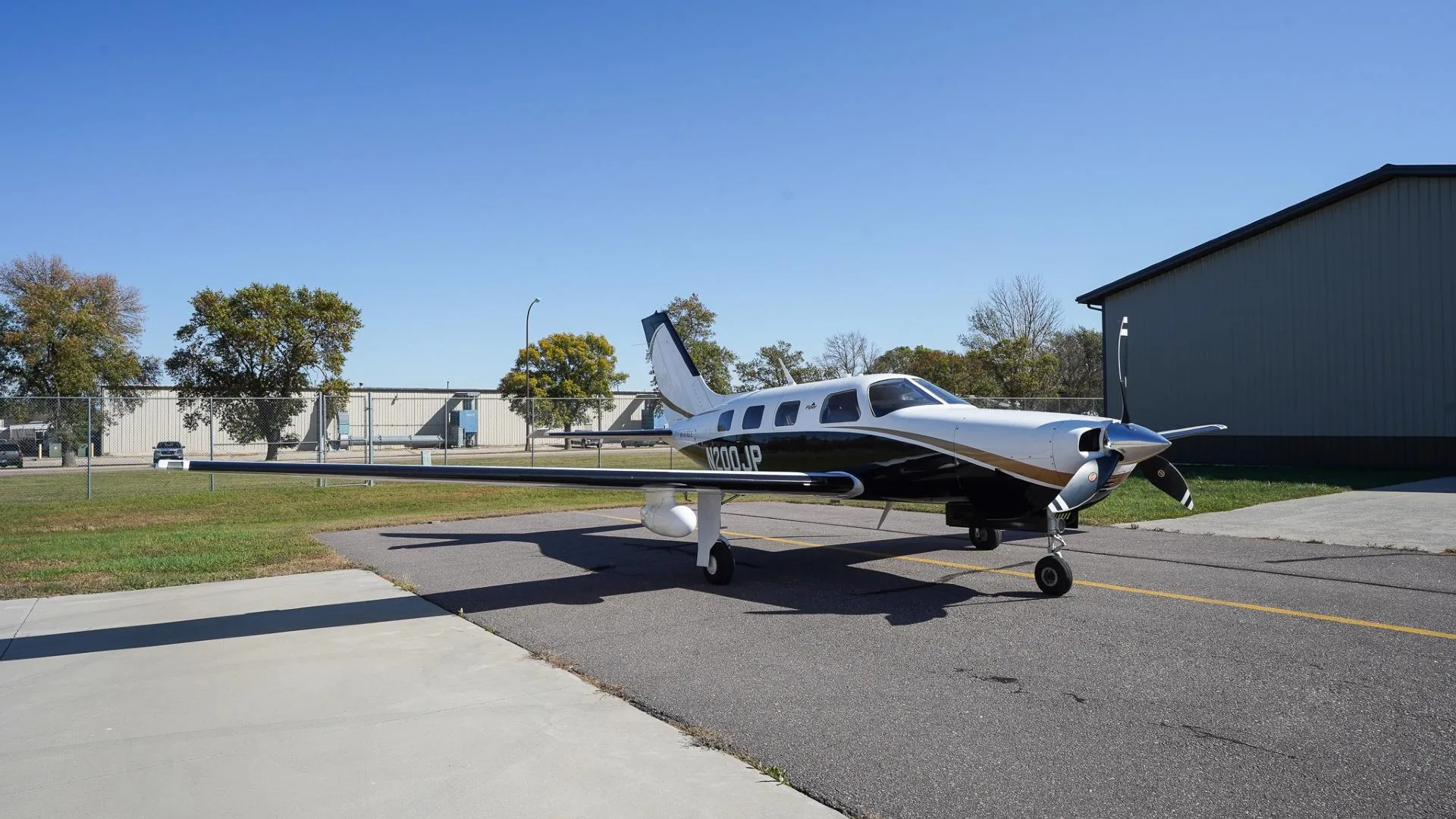 A front-side view of a white and black Piper Mirage N200JP with gold accents parked on an airfield.