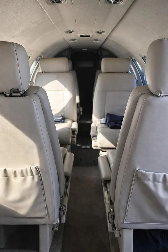 View looking forward down the aisle of a private jet cabin, showing two rows of light-colored leather seats.