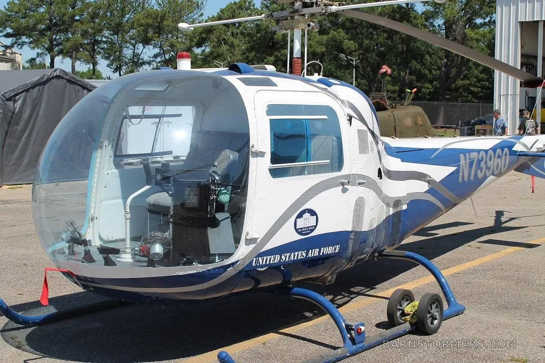 A white and blue helicopter with 'UNITED STATES AIR FORCE' text and registration N73960, parked on asphalt with trees in the background.