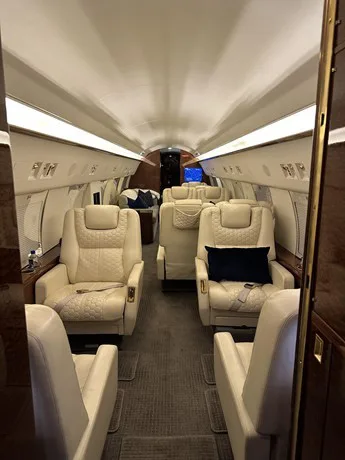 A long view down the aisle of the private jet's cabin reveals multiple rows of cream-colored quilted leather seats.