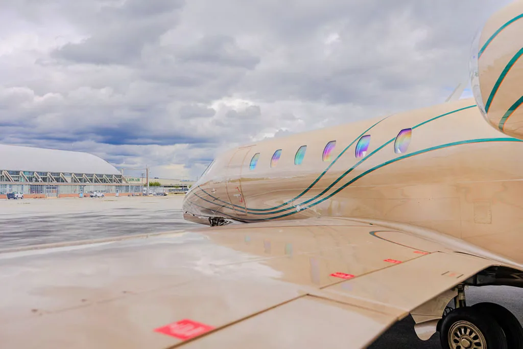 A side view of the beige business jet's fuselage and wing, showing the cabin windows and green stripe details.