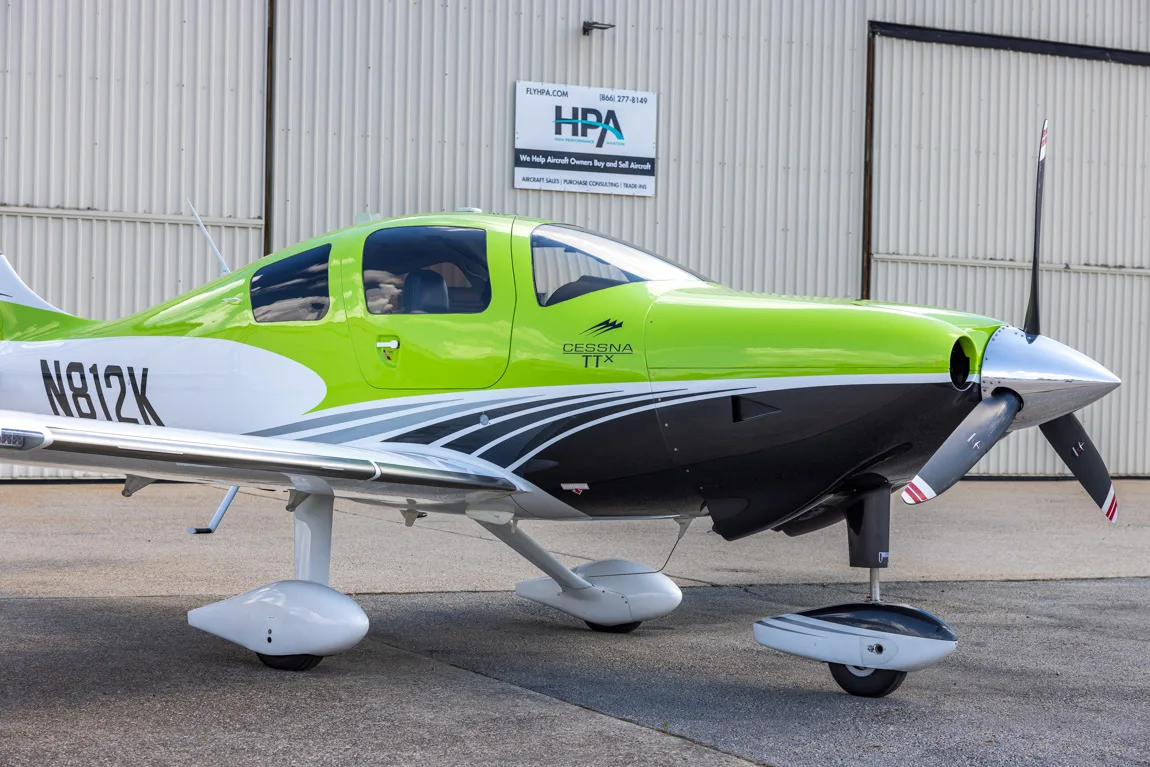 A lime green, white, and black Cessna TTX aircraft with registration N812K parked on an airfield in front of a hangar.
